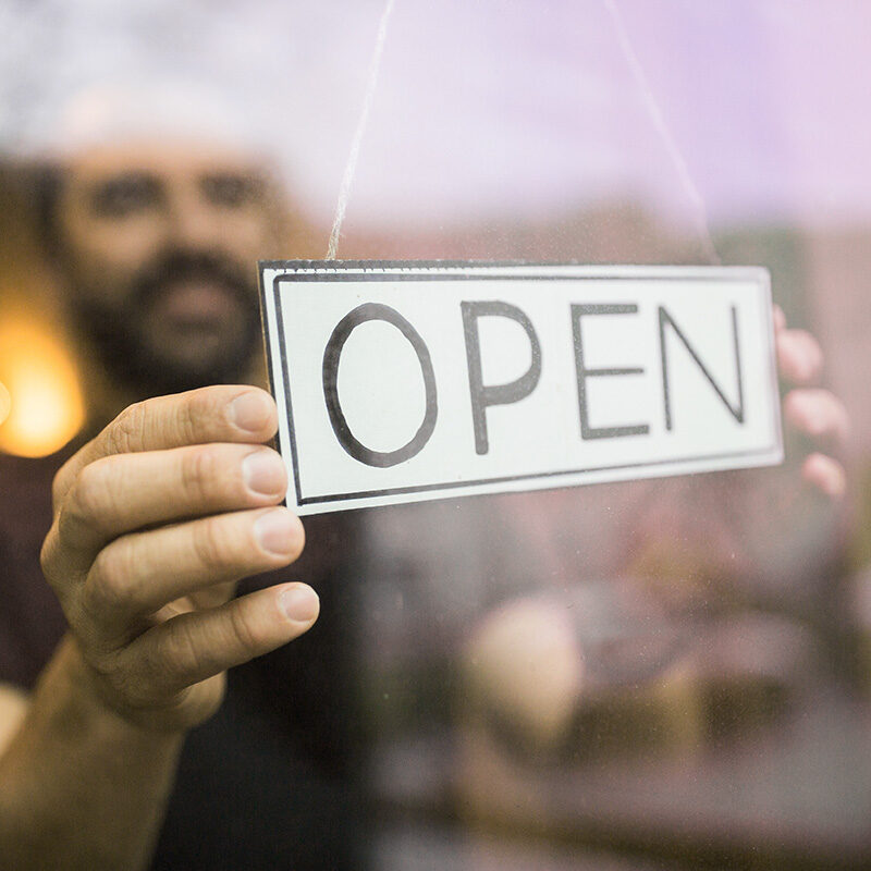 Person hanging an “OPEN” sign in a storefront window.